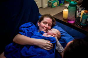 A mother cuddles with her newborn boy on a couch.